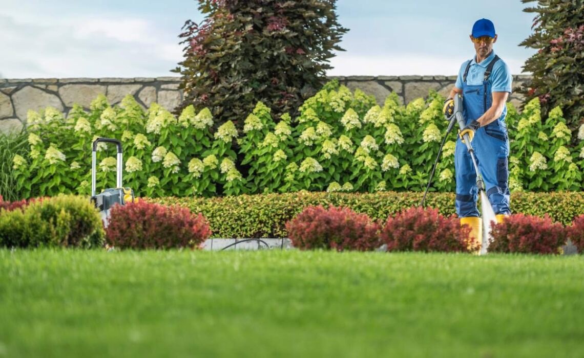 Caucasian Garden Keeper Cleaning Residential Driveway Using Professional Pressure Washer