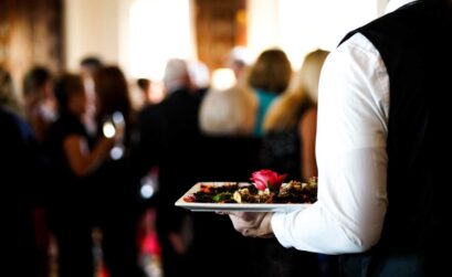 A closeup shot of a waiter's arm carrying a plate of a dish with a pink rose in it